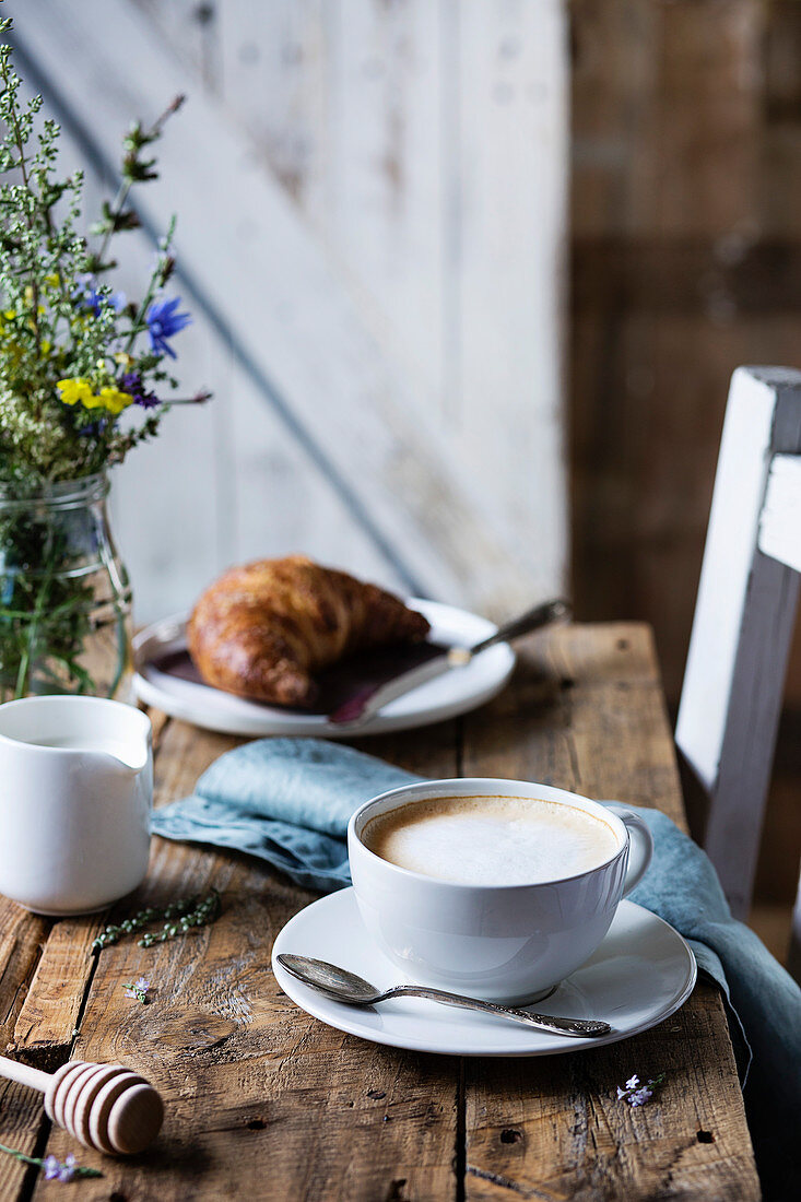 Tasse Kaffee mit Croissant auf rustikalem Holztisch in Landhausküche