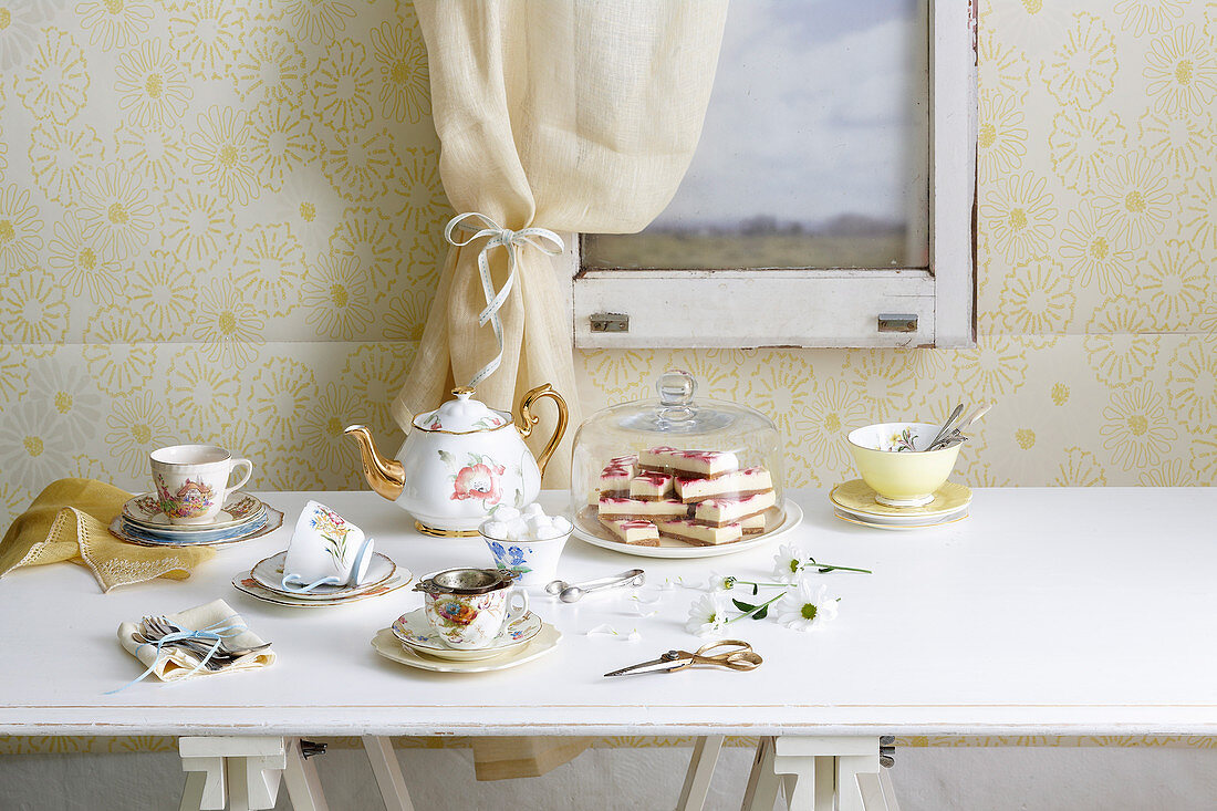 Teegedecke auf weißem Tisch und Teegebäck unter einer Glasglocke