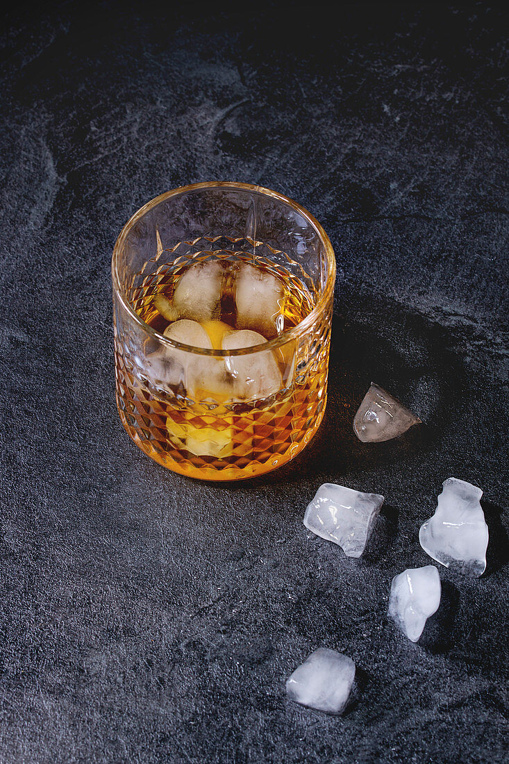 Ein Glas Scotch Whiskey mit Eiswürfeln auf grauem Untergrund