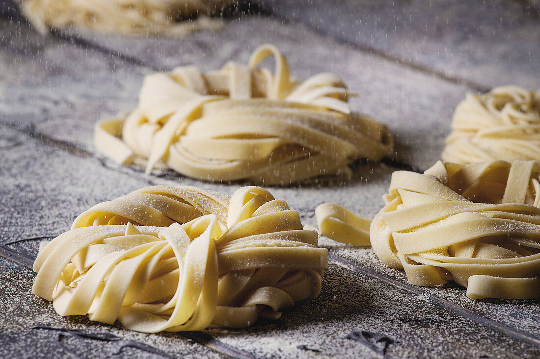 Variety of italian homemade raw uncooked pasta spaghetti and tagliatelle with sprinkling semolina flour