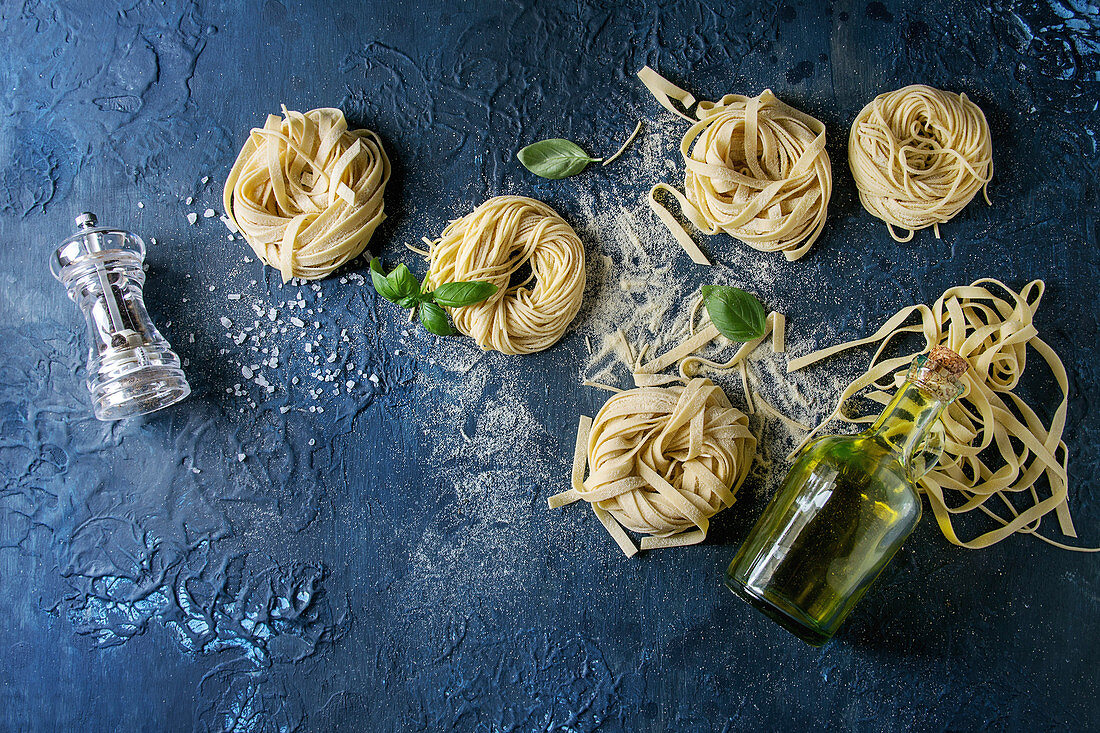 Frische Tagliatelle und Spaghetti auf dunkelblauem Untergrund (Aufsicht)