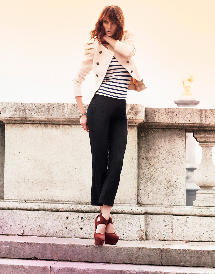 A brunette woman wearing a striped top, a light blazer and black trousers