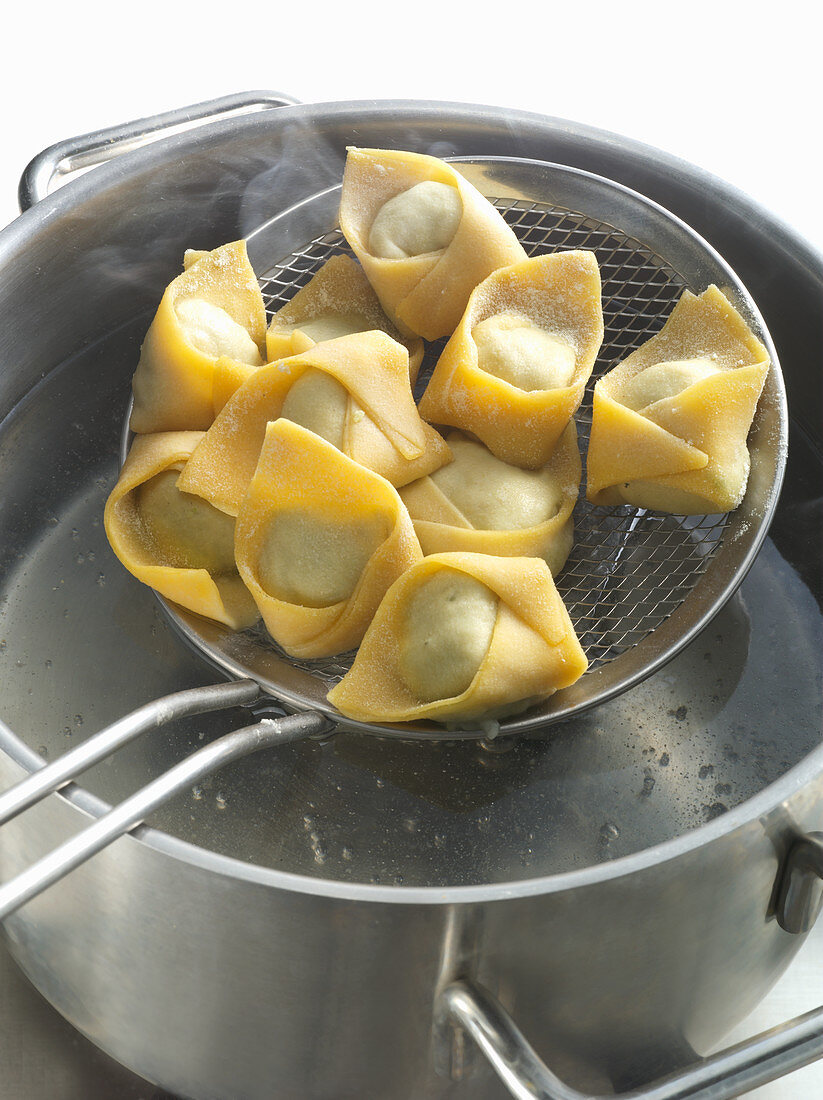 Fresh tortellini in a sieve with a pan of boiling water