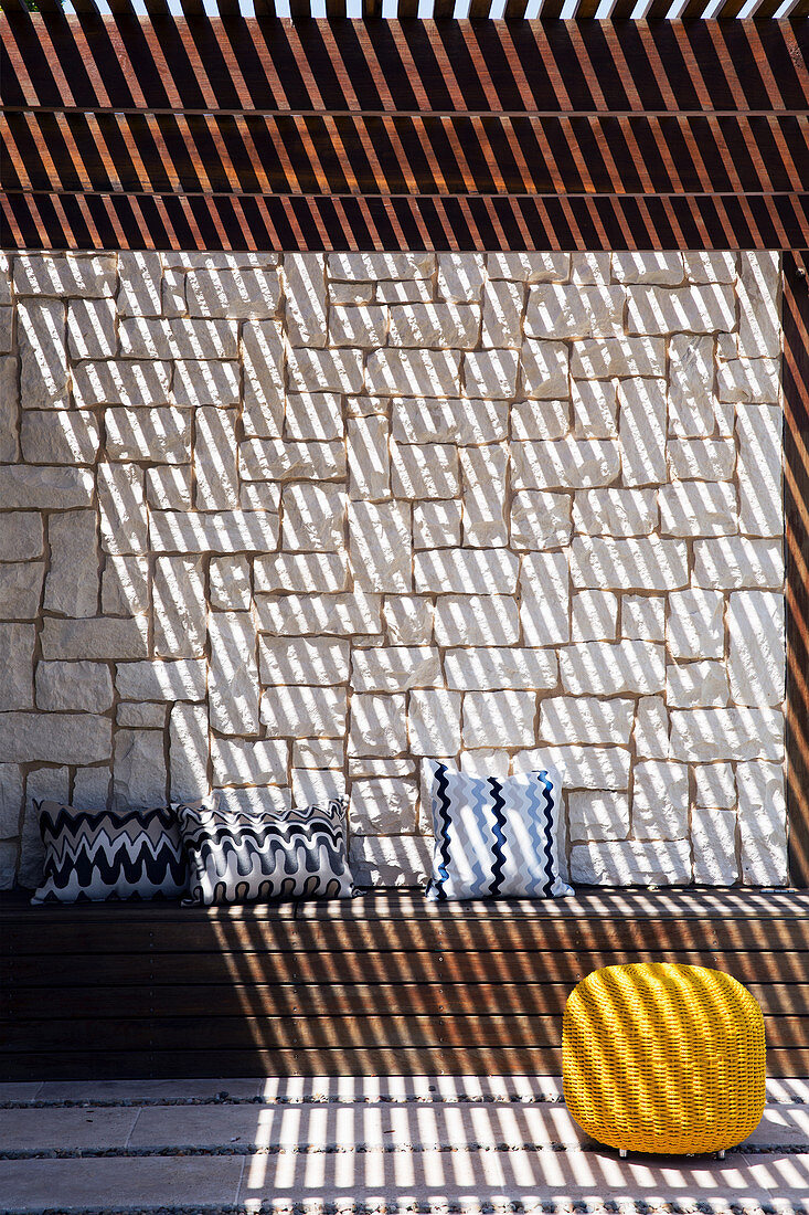 Bench with cushions and pouf under pergola with slatted roof