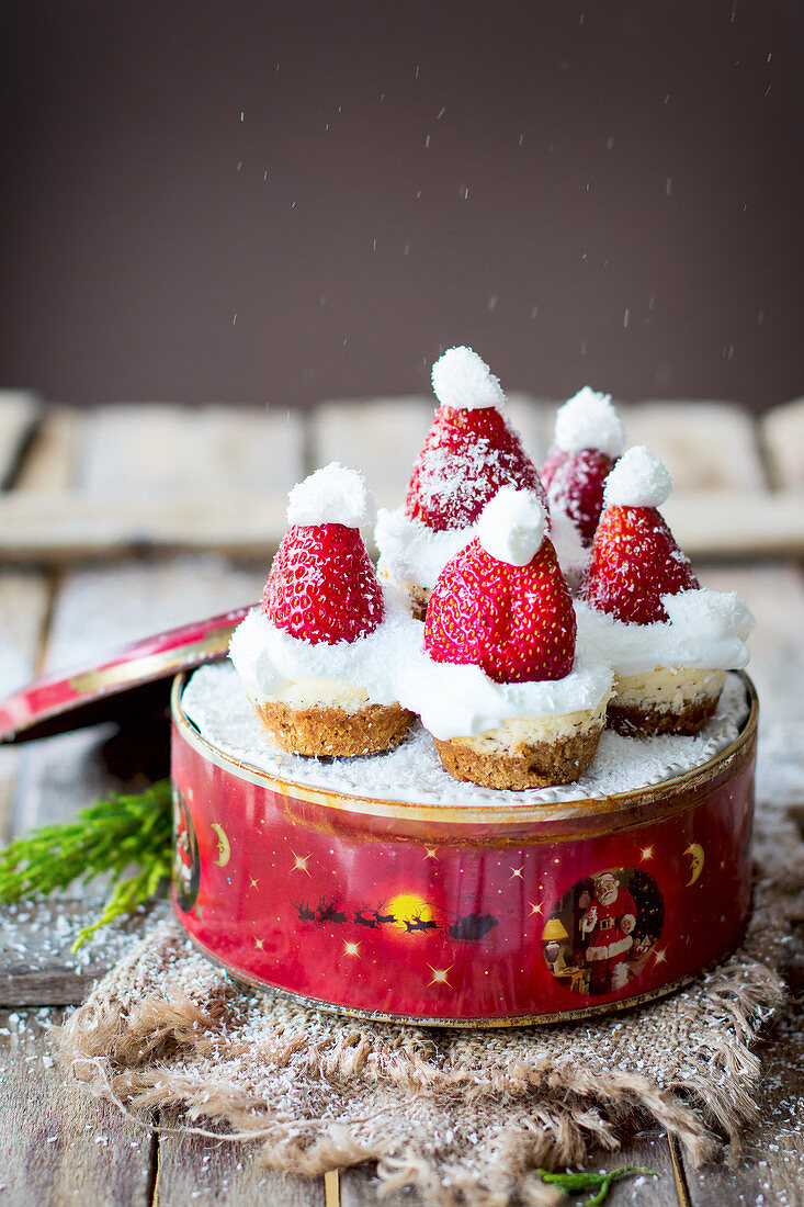 Mini-Käsekuchen in Keksdose dekoriert mit Weihnachtsmützen aus Erdbeeren