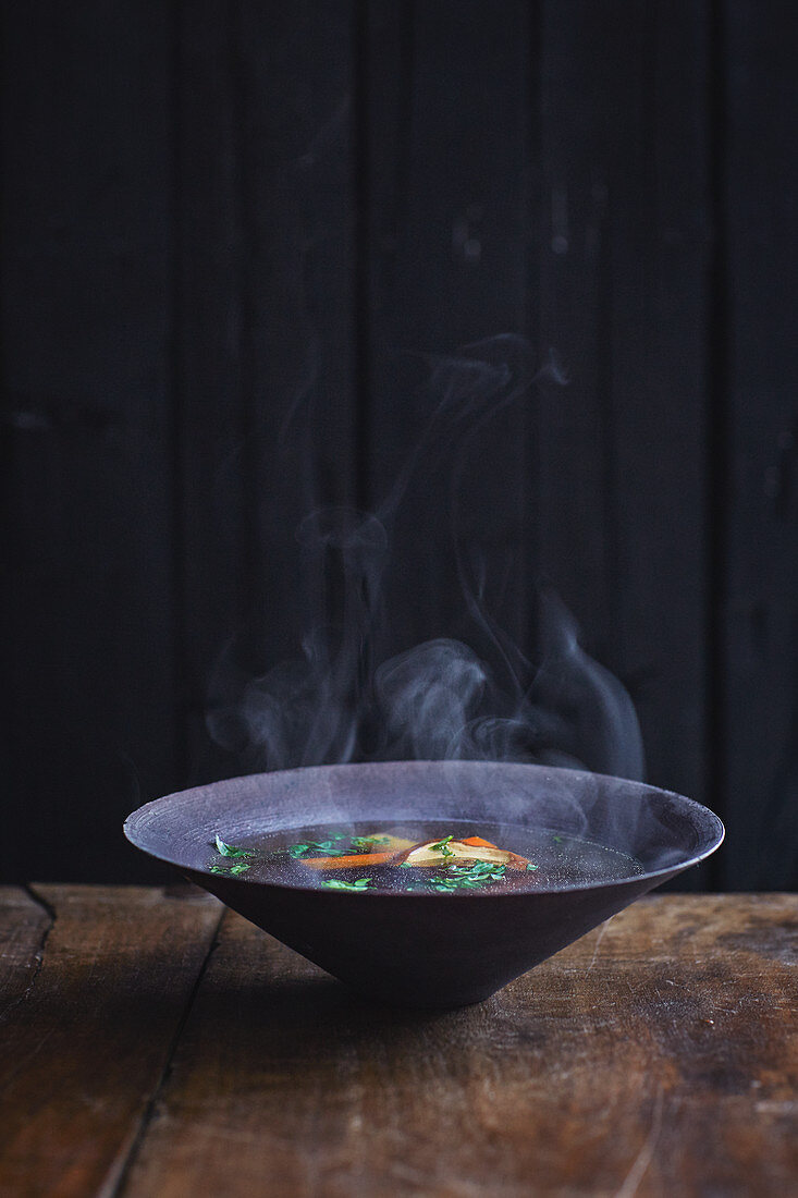 Steaming hot broth in a dark earthenware bowl