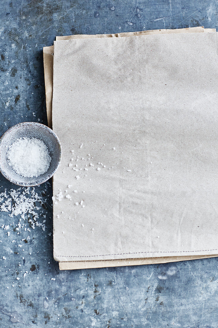 A dish of coarse sea salt next to multiple sheets of paper
