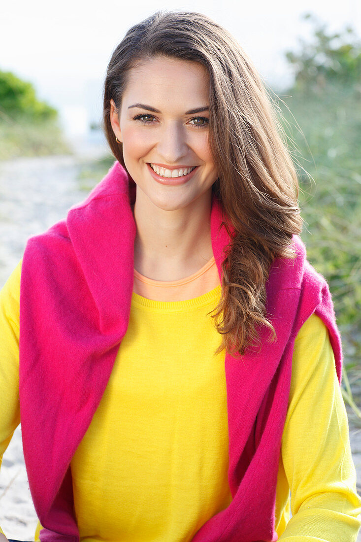 A brunette woman wearing a yellow jumper with a pink jumper over her shoulders