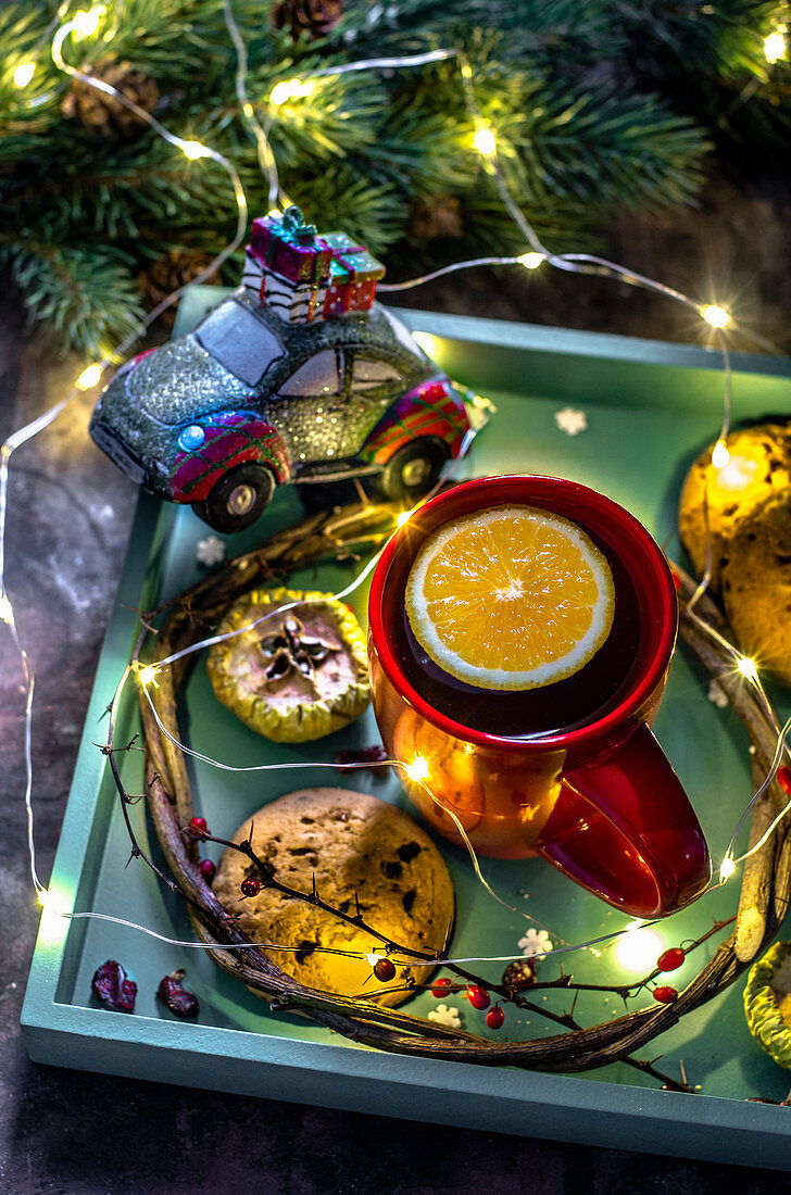Weihnachtstee mit Orange und Schokokeksen auf weihnachtlichem Tablett