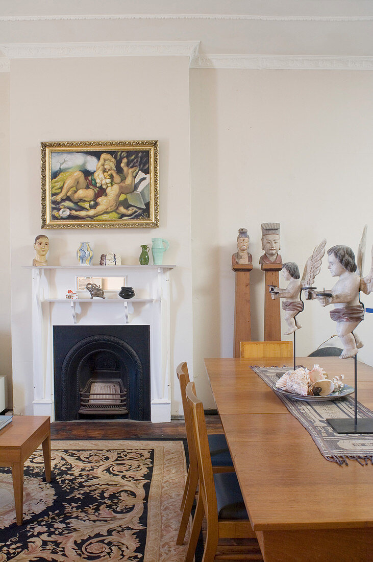 Cherubs on dining table, artworks and fireplace in open-plan interior