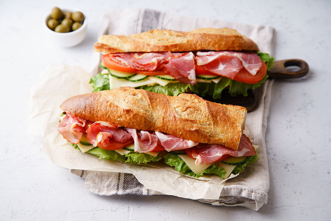 Side view of two fresh baguette sandwiches bahn-mi styled with ham, sliced cheese, tomatoes and fresh lettuce
