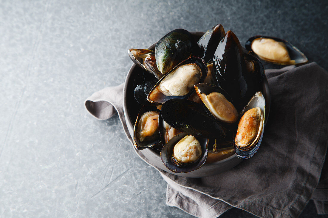Fresh mussels in black ceramic bowl on dark concrete background