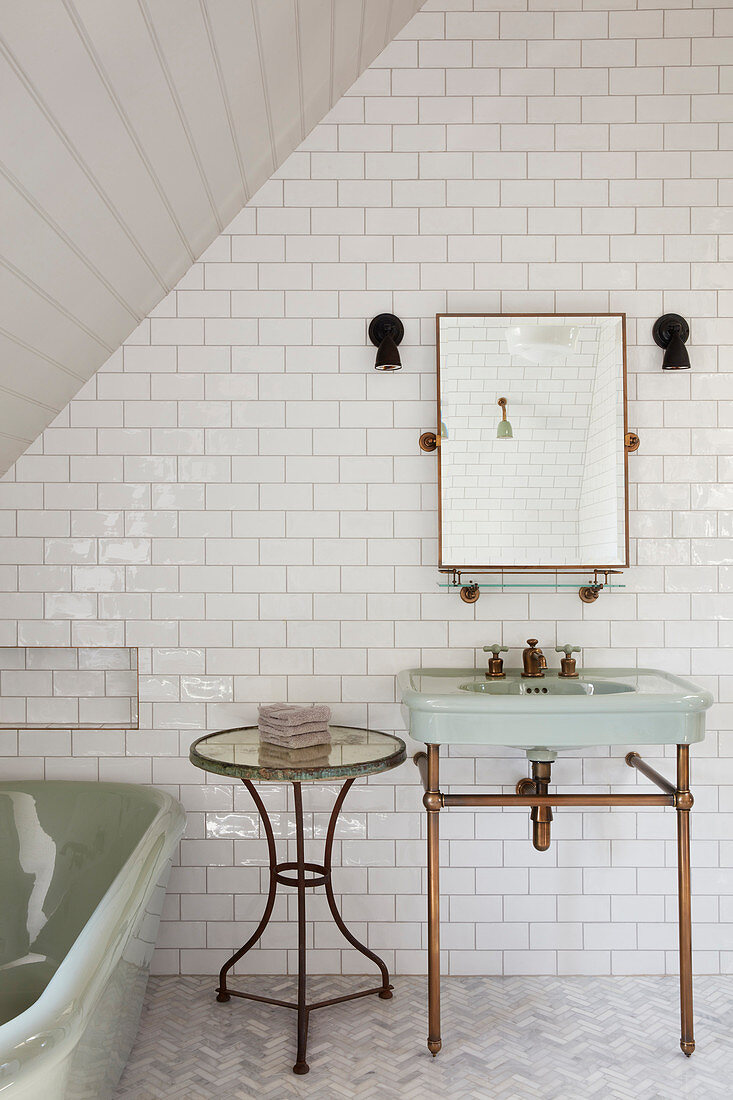 Vintage-style washstand, side table and bathtub in tiled bathroom
