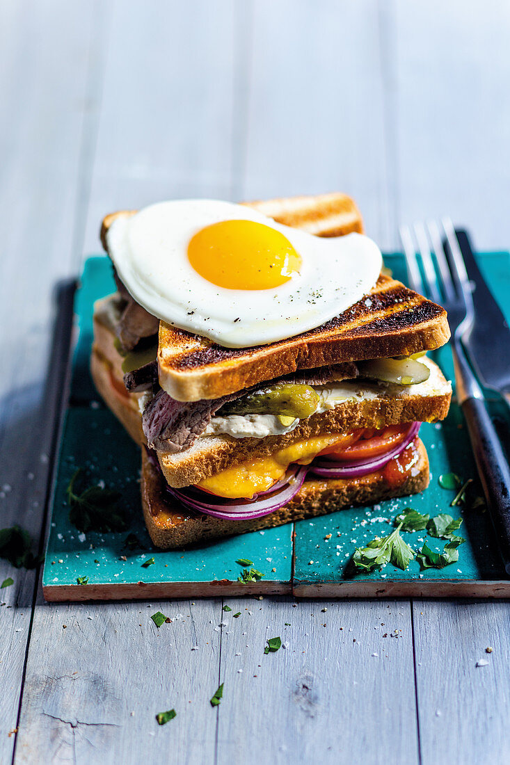 A double-decker toasted sandwich with steak and a fried egg