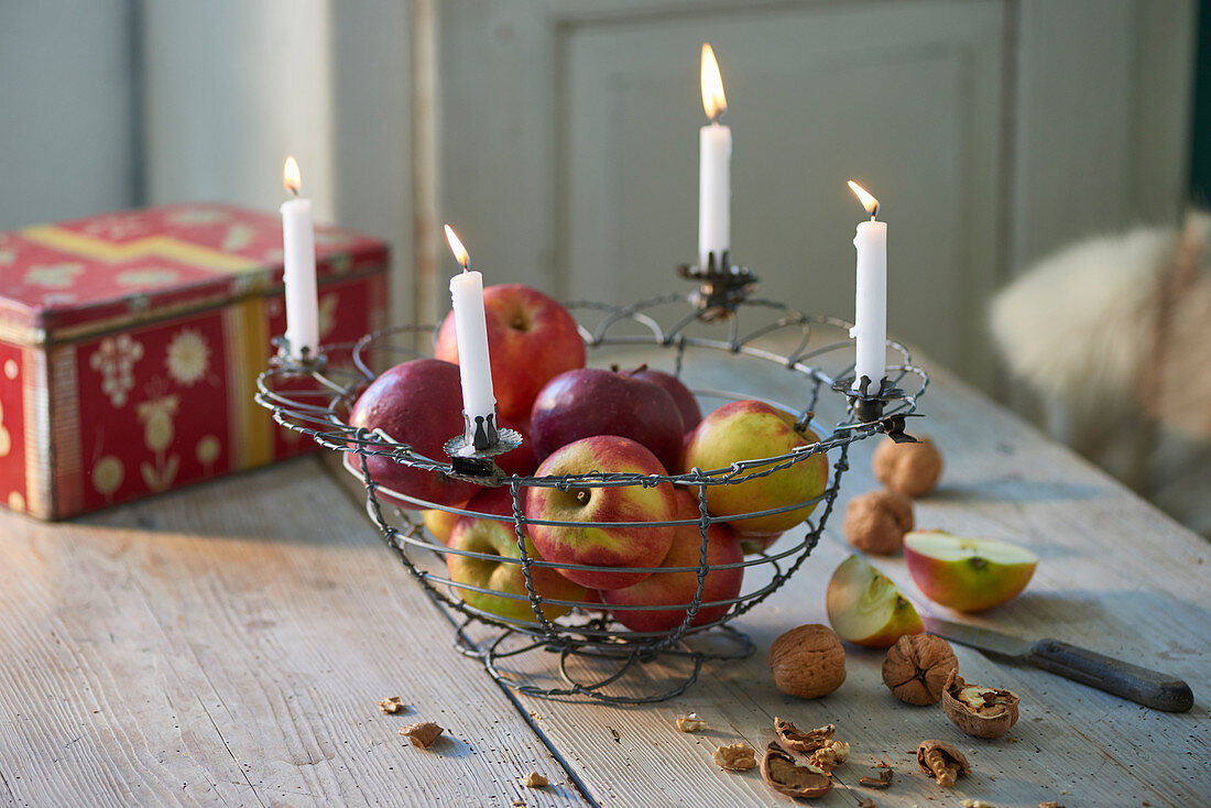 Äpfel im Drahtkorb mit vier brennenden weißen Kerzen