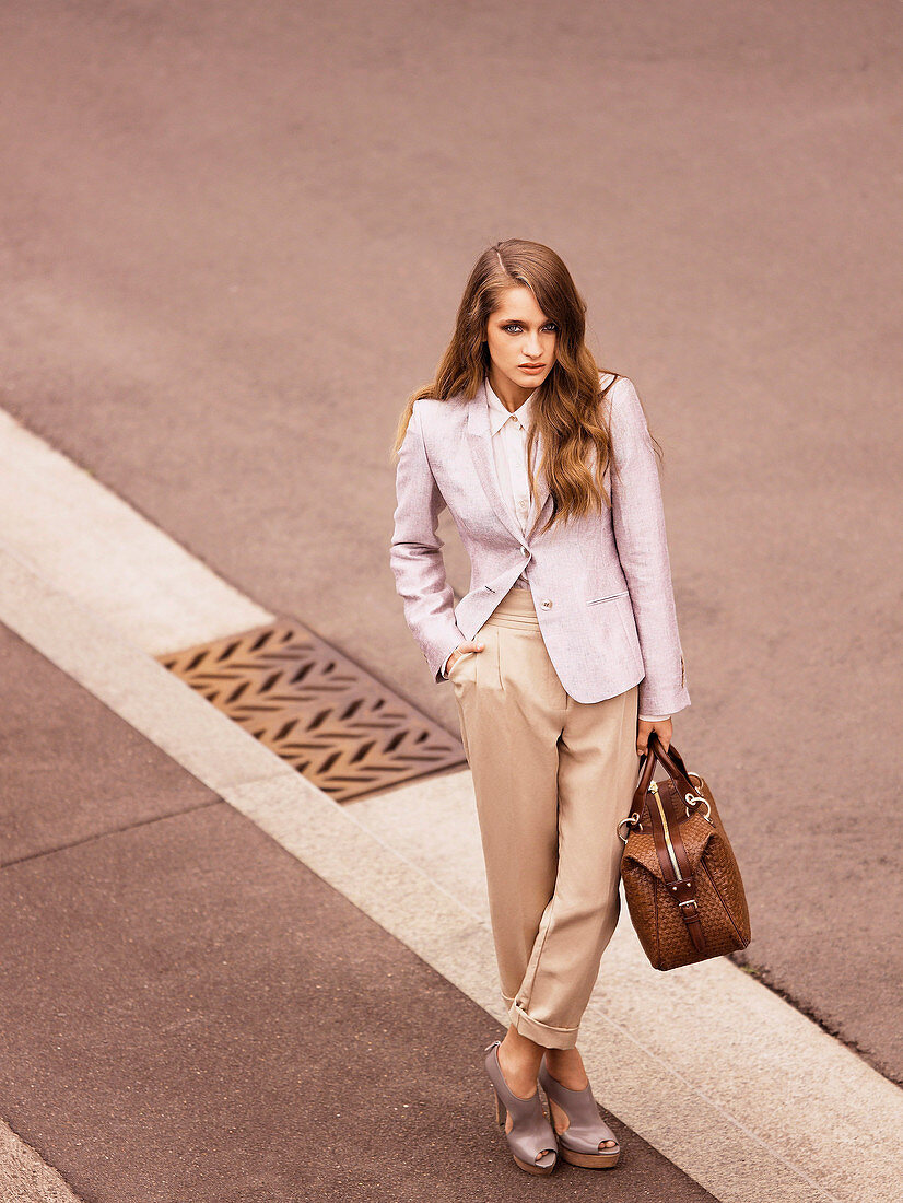 Junge Frau mit beiger Hose, rosa Blazer und Tasche