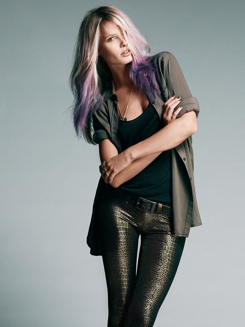 A young woman with dip-dyed hair wearing a snake-patterned trousers, a black top and a beige shirt