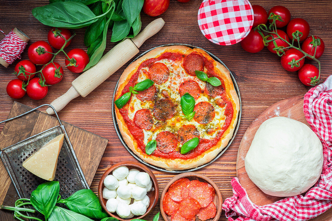 Gebackene Salamipizza und Zutaten auf Holztisch