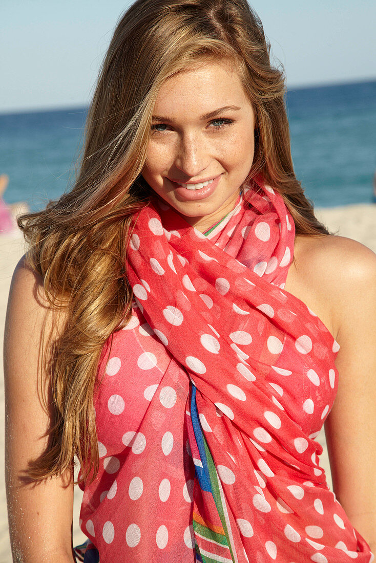 A young blonde woman by the sea wearing a beach towel