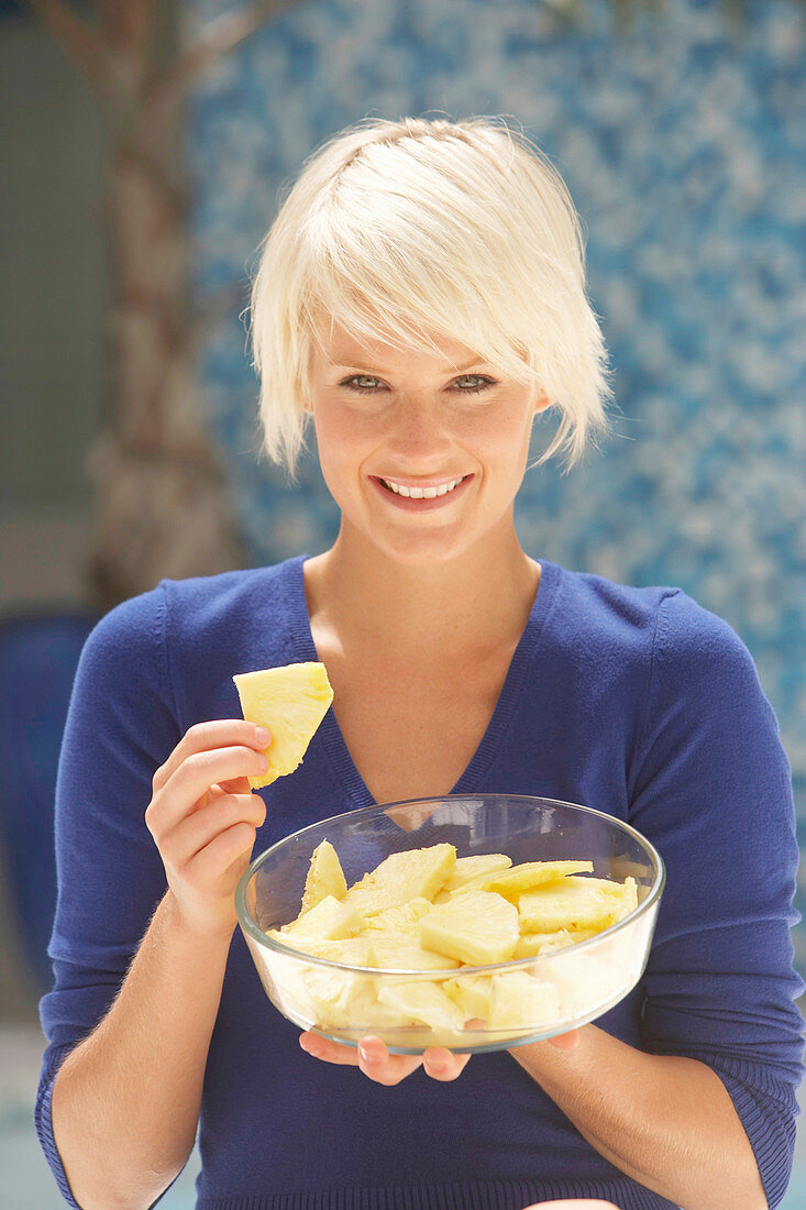 Reife, kurzhaarige blonde Frau im blauen Shirt mit einer Schale Ananas