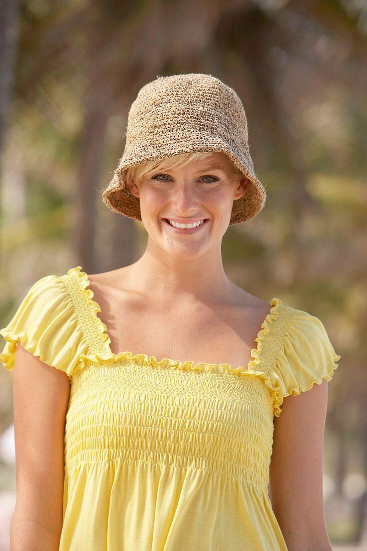 A mature blonde woman with short hair outside wearing a yellow top and a hat