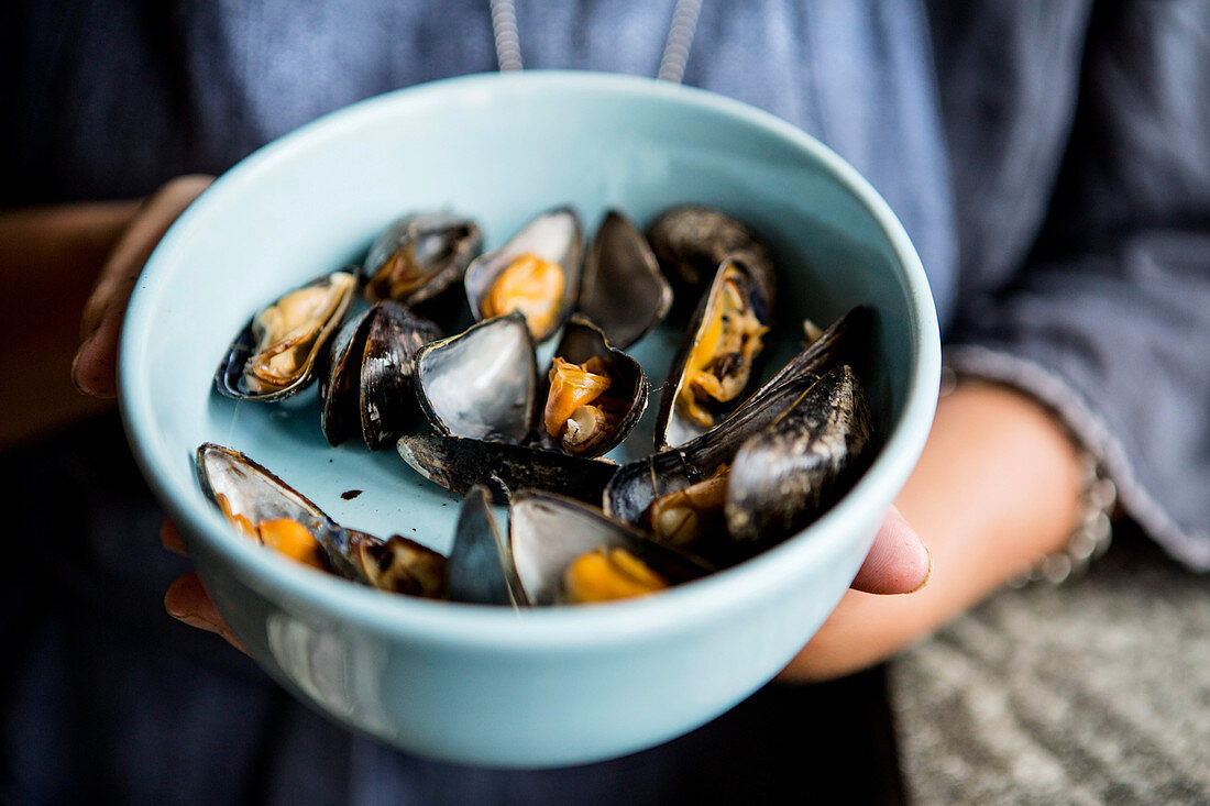A woman holding a bowl of grilled mussels