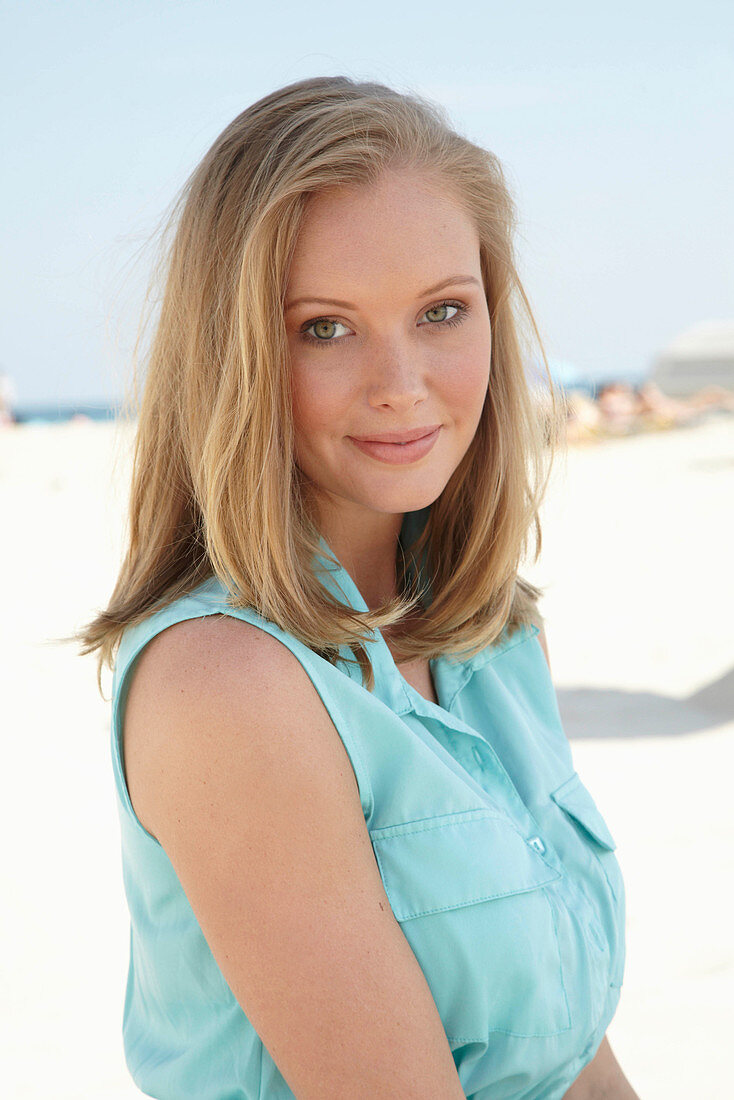 A young blonde woman on a beach wearing a light-blue summer dress