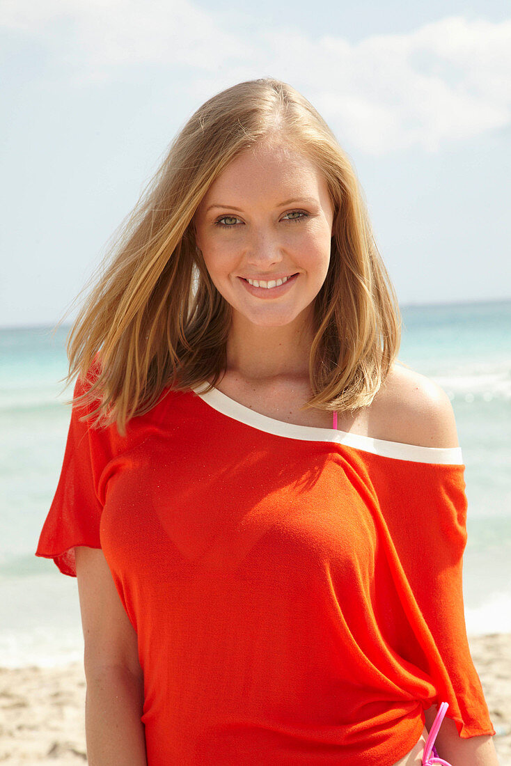 A young blonde woman on a beach wearing a purple bikini and an orange top