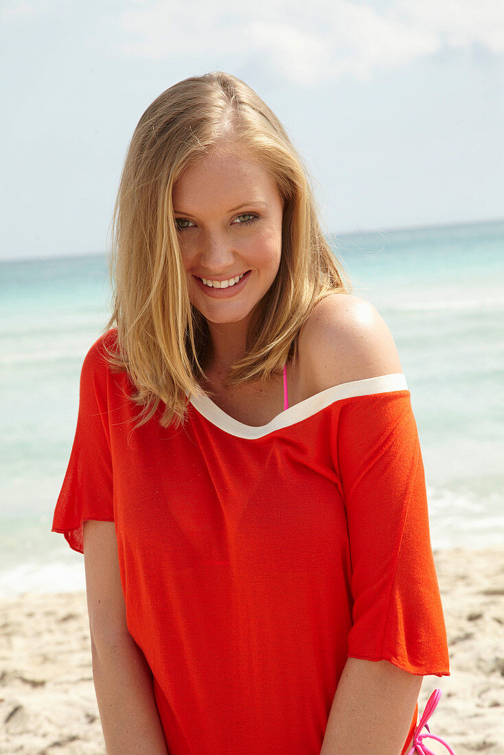 A young blonde woman on a beach wearing an orange top