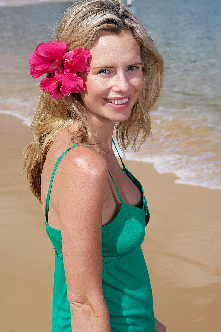 Junge blonde Frau mit Blume im Haar im grünen Top am Strand
