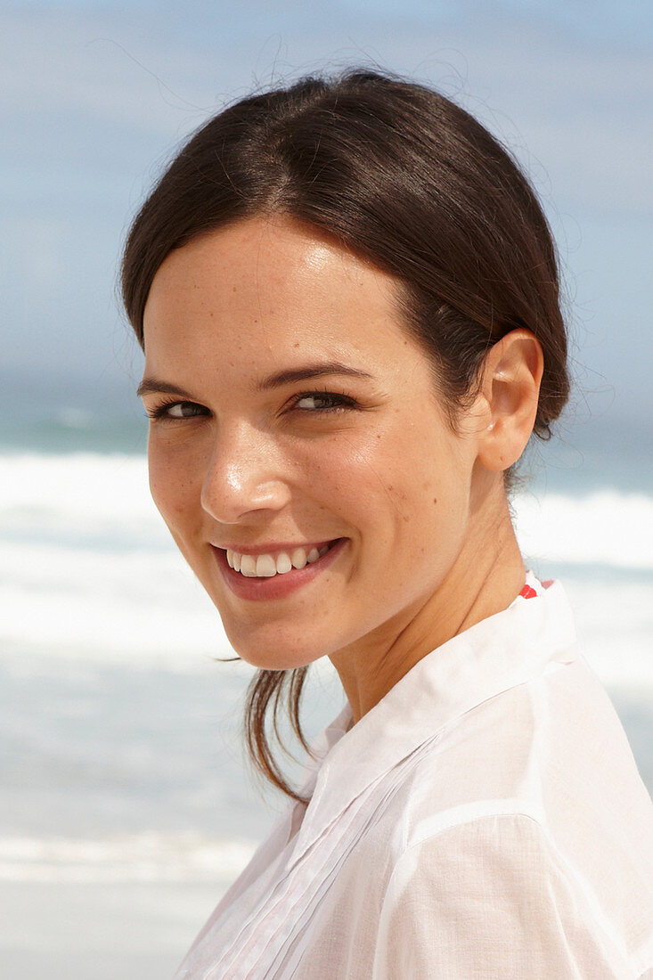 A young brunette woman on a beach wearing a white summer dress