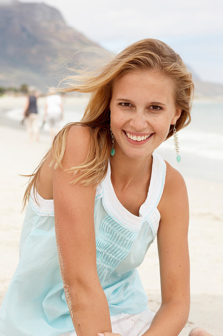 A young blonde woman on a beach wearing a light-blue top