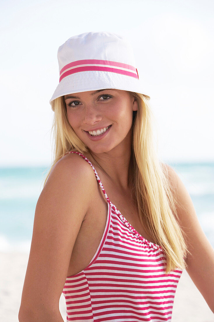 Junge blonde frau im rot-weiß gestreiften Shirt und mit weißem Hut am Strand
