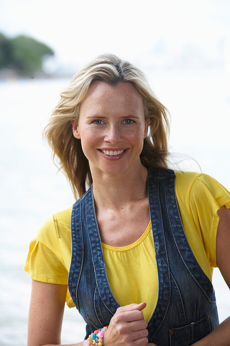 Junge blonde Frau mit gelbem Shirt und Jeansweste im Strand