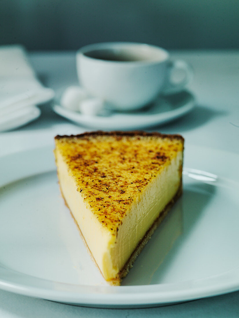 A slice of custard tart or French flan with cup of coffee