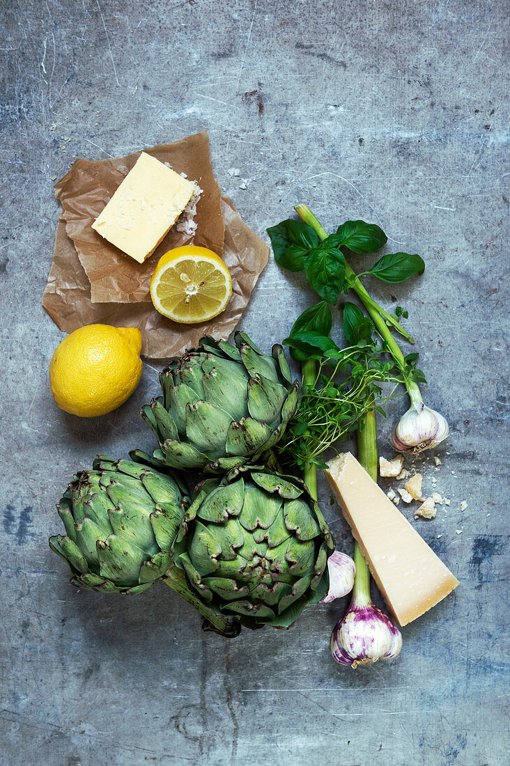 An arrangement of ingredients with artichokes, butter, lemon, garlic and cheese