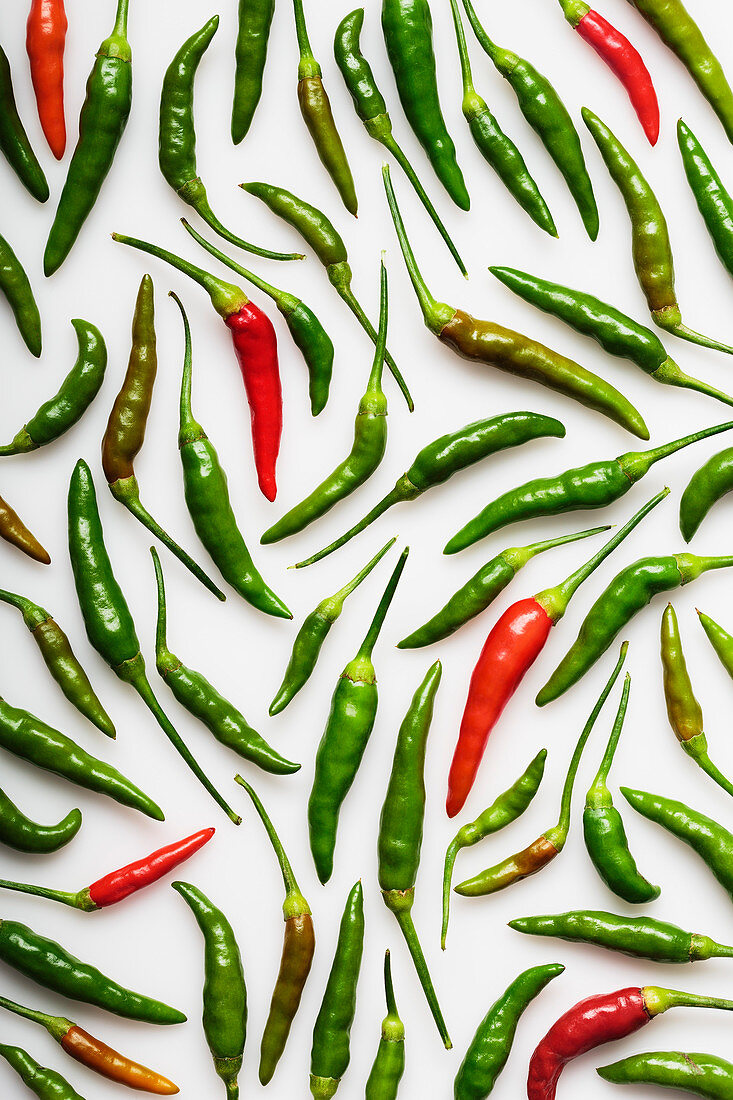 Green and red Thai chili peppers on a white background