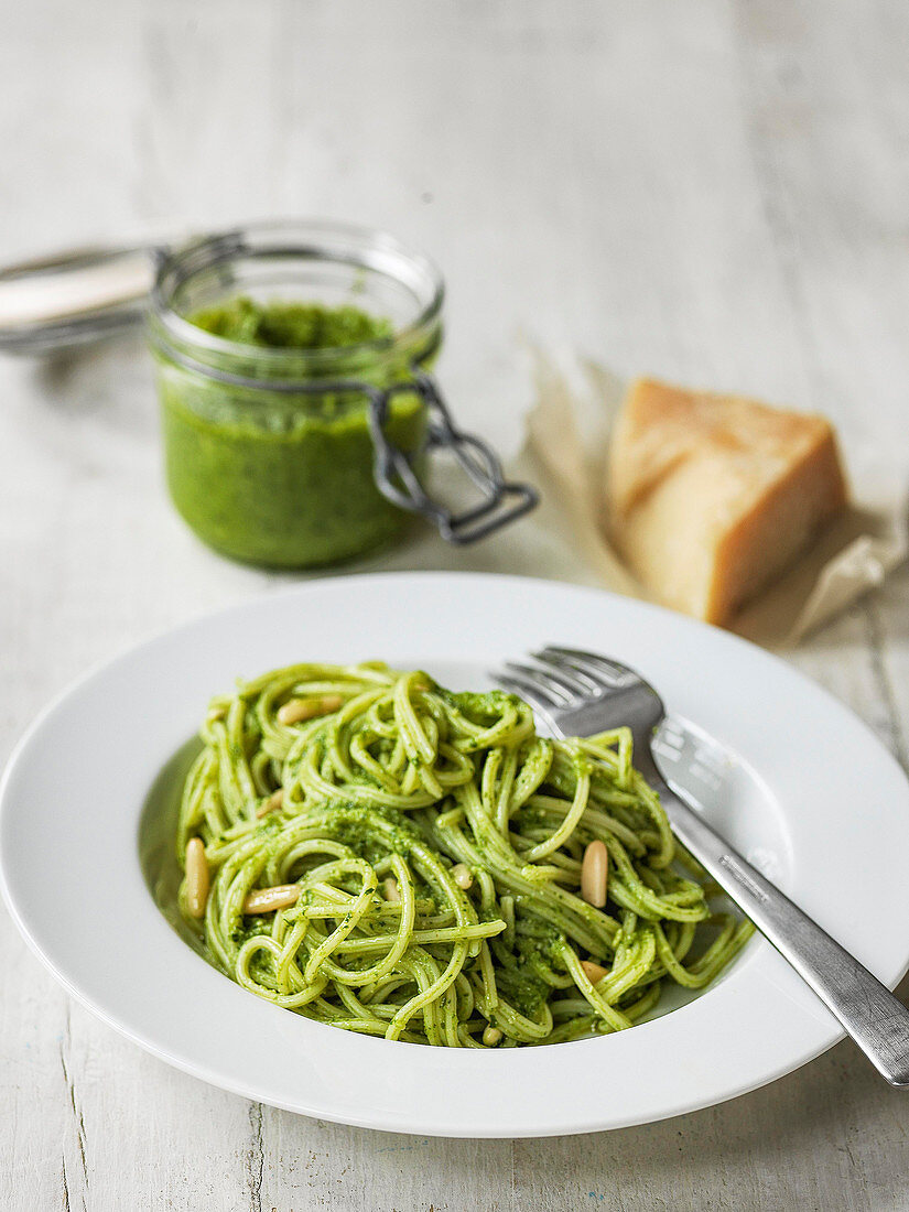 Spaghetti with pesto and pine nuts with jar of pesto and parmesan behind