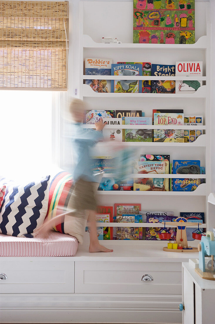 Boy walking in front of book shelves in child's bedroom