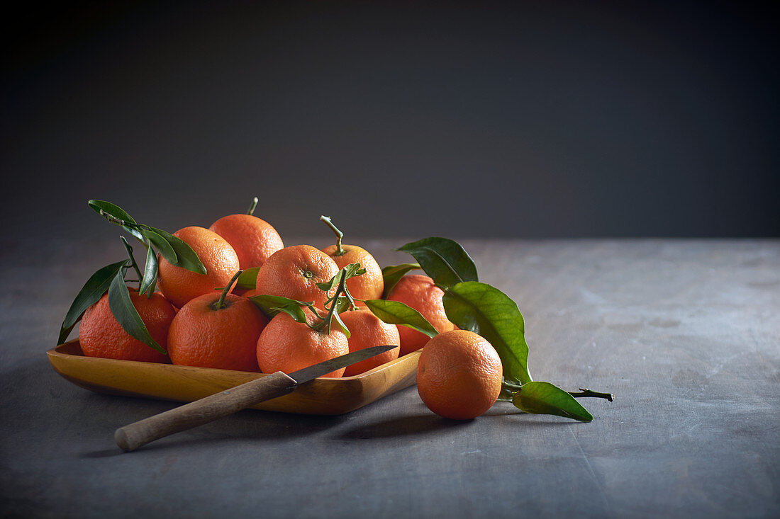Mandarins with leaves in a wooden bowl with a paring knife