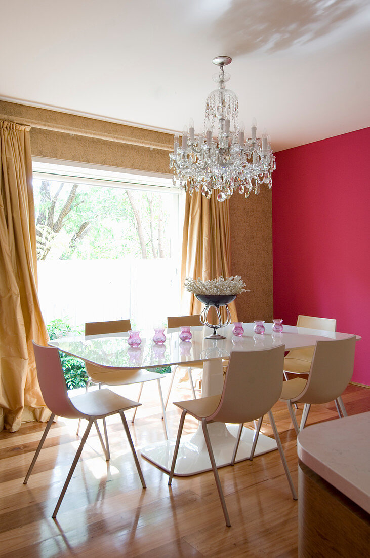Designer dining table and chairs below chandelier in dining room with hot-pink wall