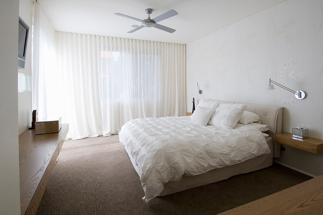 Double bed with white bedspread and pillows and wall-mounted lamps above floating bedside tables in bedroom