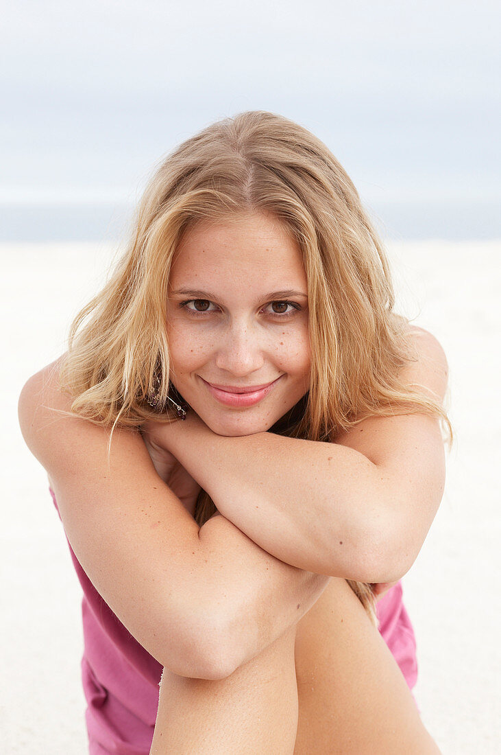 A young blonde woman on a beach wearing a pink top and a bikini