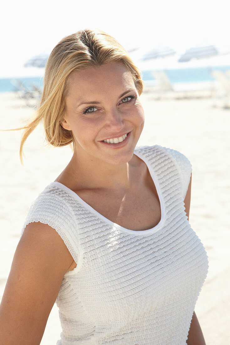 Reife blonde Frau im weißen Top am Strand