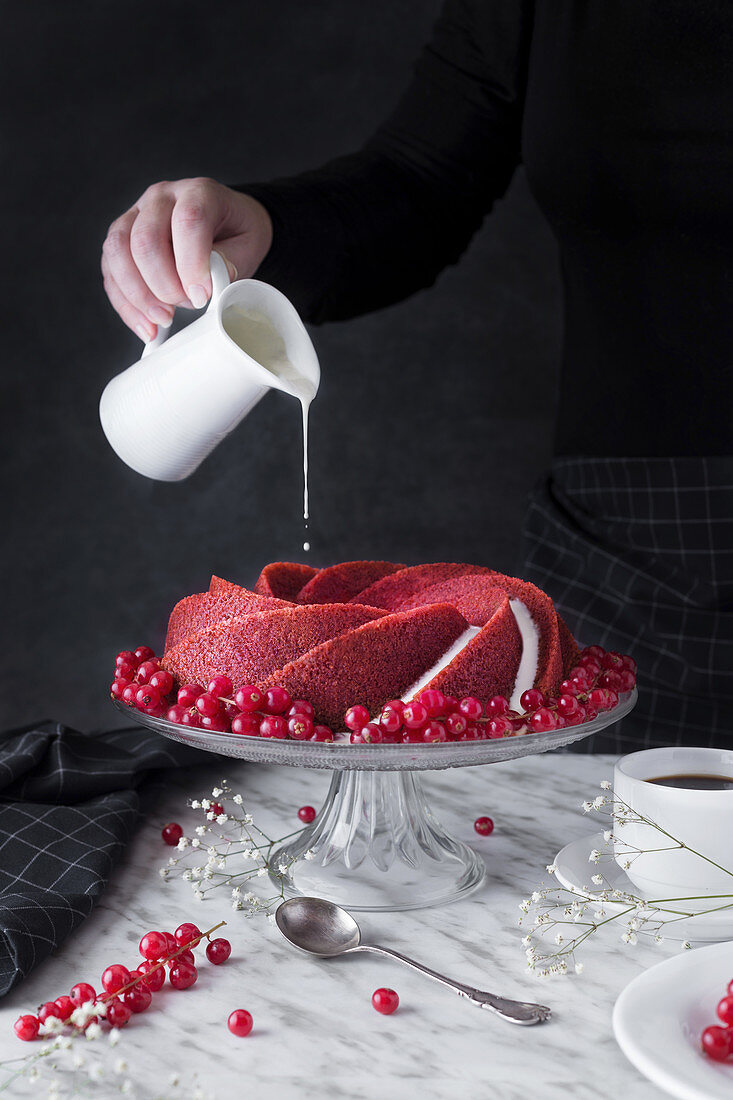 Frau giesst Sahne auf Red Velvet Cake