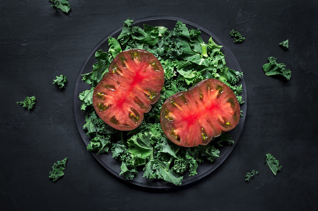 Half-cut red tomato on kale salad