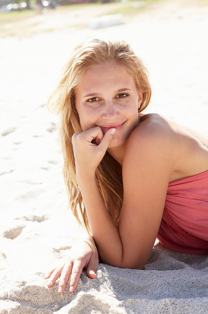 A young blonde woman on a beach wearing a pink top