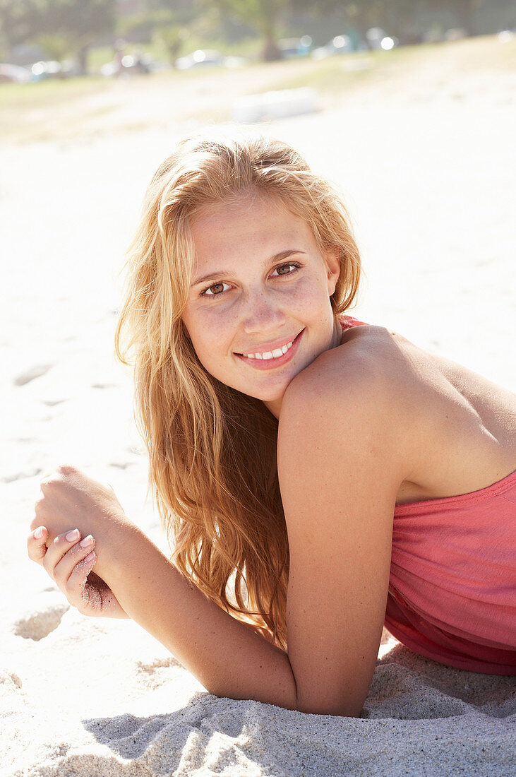 A young blonde woman on a beach wearing a pink top