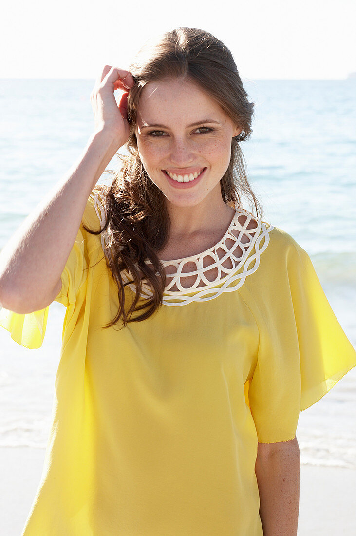 Junge brünette Frau im gelben Sommerkleid am Strand