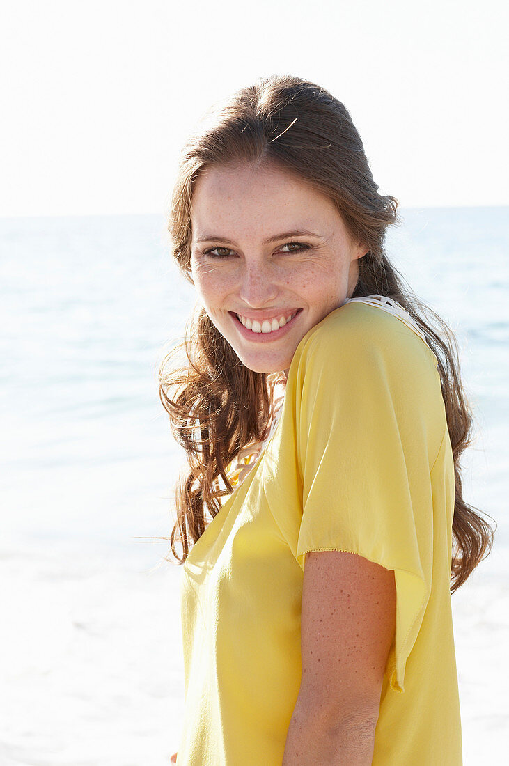 A young brunette woman on a beach wearing a yellow summer dress